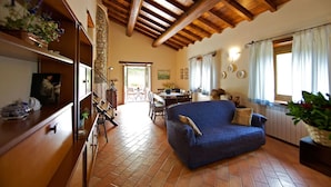 A spacious living room with a blue sofa, wooden beams on the ceiling, a dining area with a table and chairs, and a kitchen area with a stove. - Wonderful private villa for 10 people with private pool, WIFI, TV, terrace, pets allowed and par... (Castel San Niccolo)