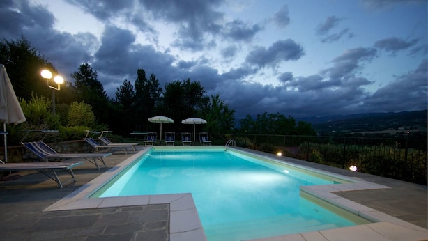 A rectangular swimming pool with a stone border, surrounded by lounge chairs and umbrellas, set against a backdrop of trees and a cloudy sky. - Wonderful private villa for 10 people with private pool, WIFI, TV, terrace, pets allowed and par... (Castel San Niccolo)