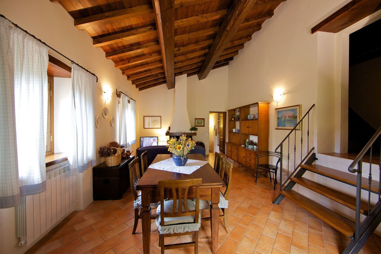A dining area with a wooden table and chairs, a vase of flowers, and a staircase leading to an upper level.