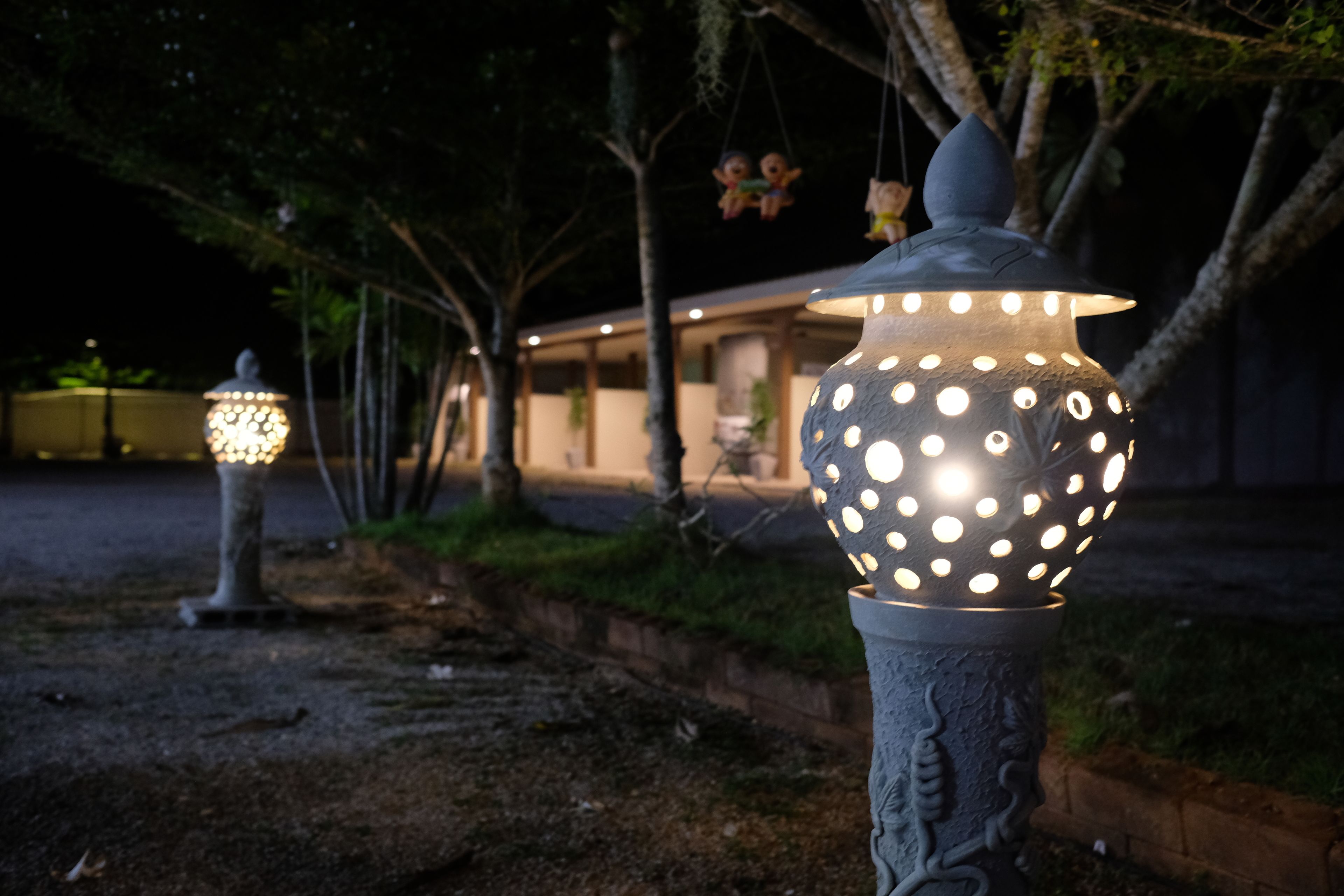 Un jardín con dos faroles iluminados, un sendero y un edificio al fondo.