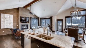 A modern kitchen with a large island, wooden flooring, and a view of a snowy landscape through large windows. - River Run Townhomes by Vail Resorts (Keystone)