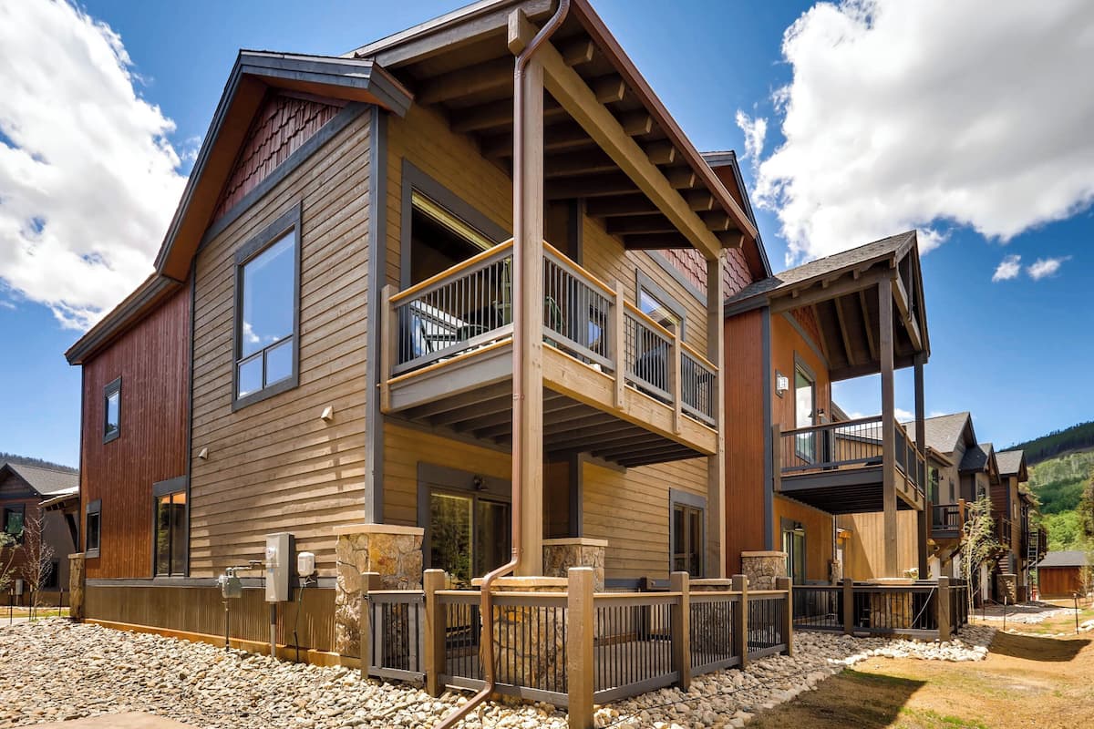 Une maison moderne à deux étages, dotée d’un balcon, de fondations en pierre et d’une terrasse en bois.