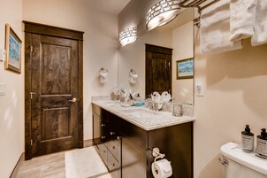 Un baño con puerta de madera, un lavabo con espejo y dos botellas de jabón Lather sobre el mueble.