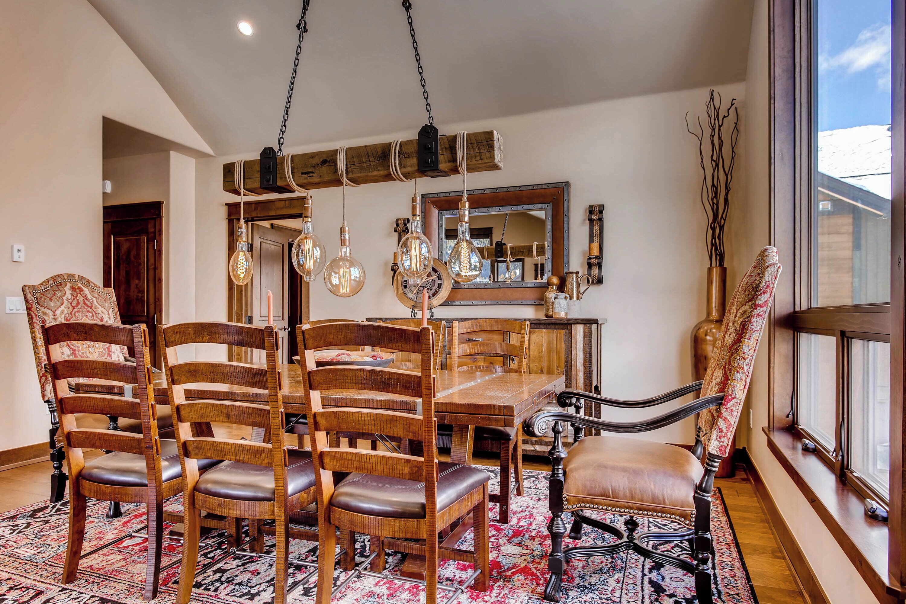 A dining area with a wooden table and chairs, hanging light fixtures, and a large mirror.
