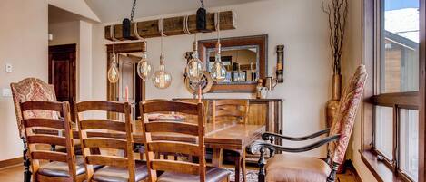 A dining area with a wooden table and chairs, hanging light fixtures, and a large mirror.
