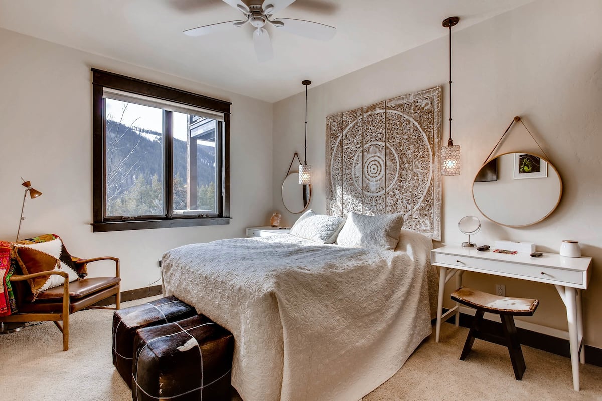 Une chambre à coucher comprenant un lit, un bureau, une chaise, un banc, une fenêtre et un ventilateur de plafond.