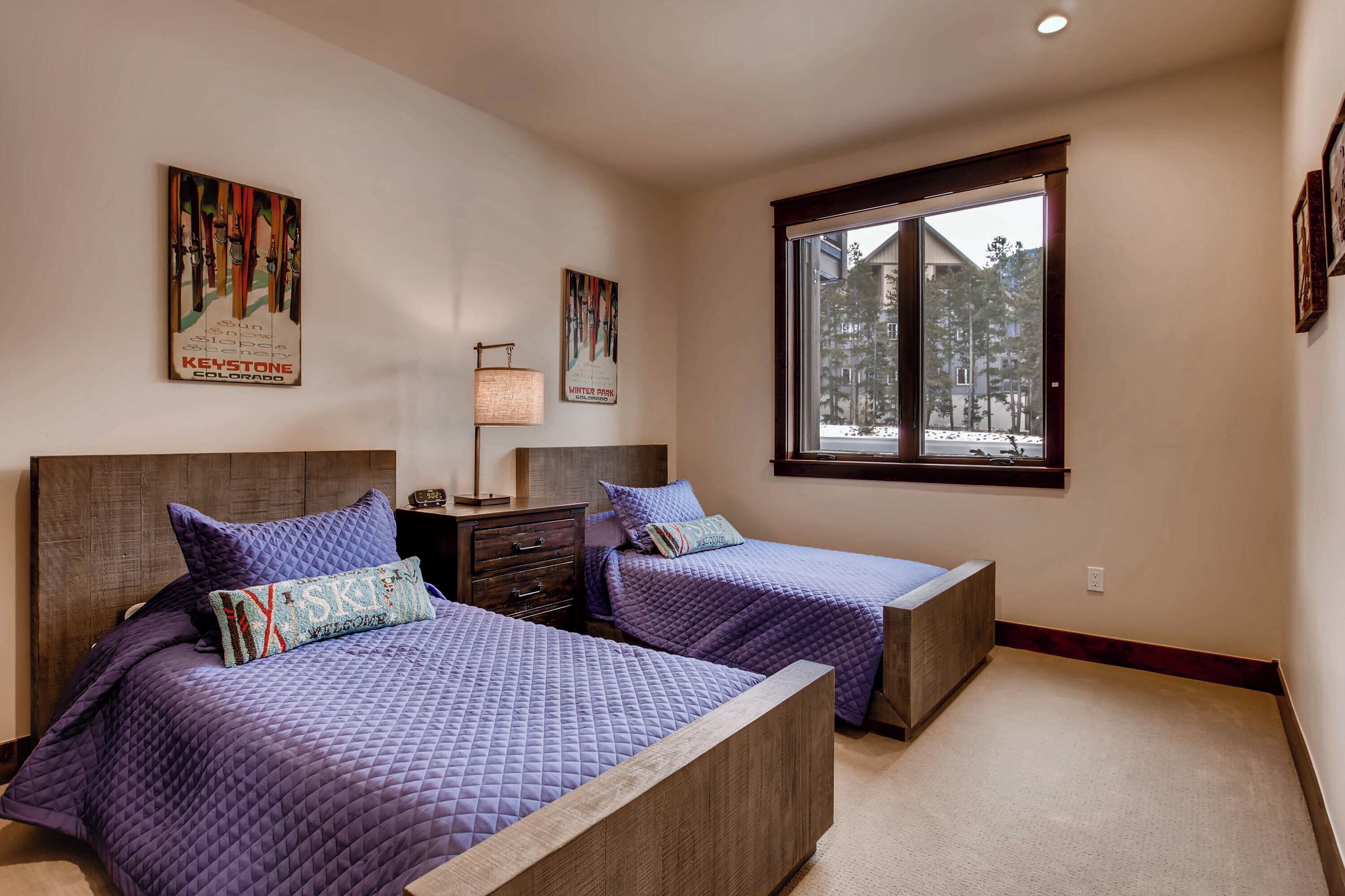 A bedroom with two beds, a window with a view of trees, and artwork on the walls.
