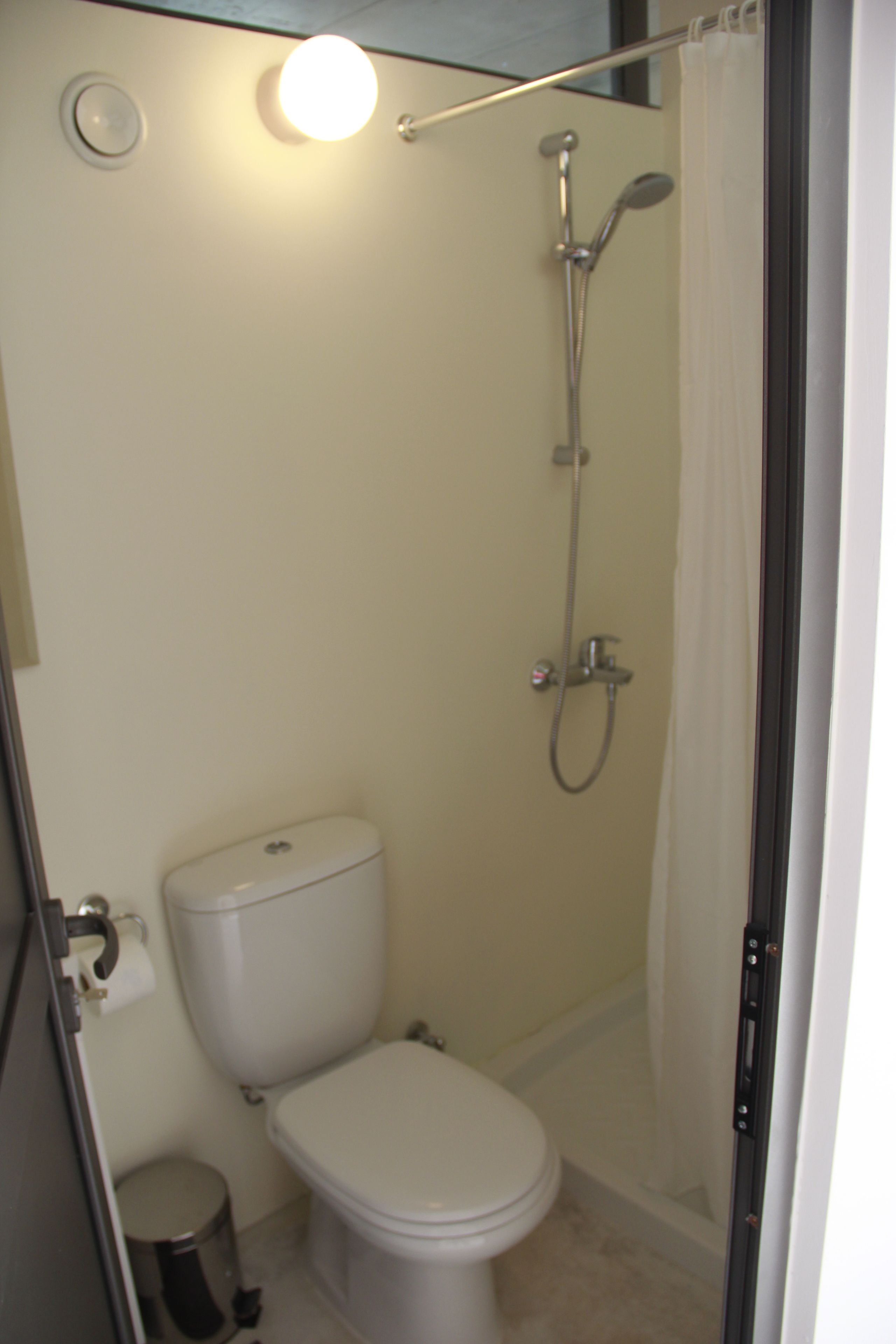 A small, enclosed bathroom with a toilet, a shower, and a toilet paper holder.