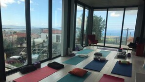 A spacious room with large windows offering a view of the landscape, multiple yoga mats, and a few chairs. - Marmaras (Lysos)