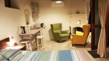 Een slaapkamer met een bed, een groene fauteuil, een gele fauteuil, een klein krukje en een open haard.