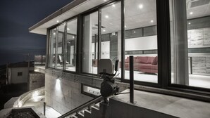 A modern building with large glass windows, a staircase leading to an upper level, and a red couch visible inside. - Marmaras (Lysos)