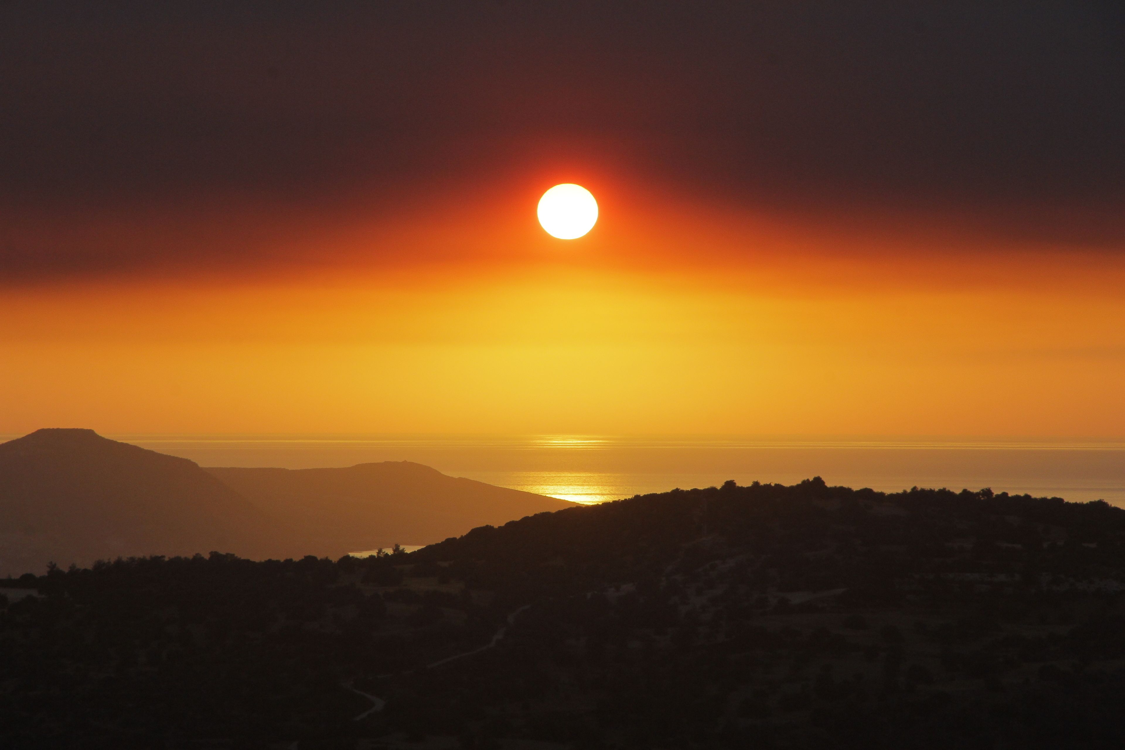 A sunset over a mountainous landscape with a view of the sea.