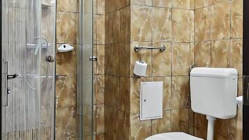 A bathroom with a glass-enclosed shower, a toilet, and a marble-tiled wall.