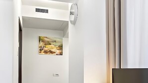 Ein Hotelzimmer mit einem Holztisch, einem Flachbildfernseher, einer Lampe, einem Bild an der Wand und einem Bett mit einem gemusterten Teppich.