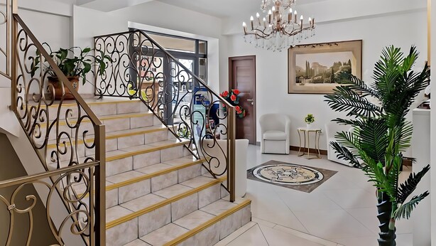 Eine Treppe mit aufwendiger Metallgalerie, einem Kronleuchter und einem großen gerahmten Gemälde an der Wand.