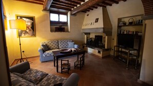 A cozy living room with a patterned sofa, a wooden coffee table, a fireplace, and a television on a stand. - Private Villa with AC, private pool, WIFI, TV, terrace, pets allowed, parking, close to Arezzo (Castiglion Fiorentino)