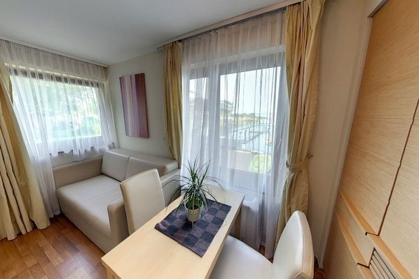 A modern room with a sofa, a dining table, and a potted plant. - Royal Mediterran Hotel (Siófok)