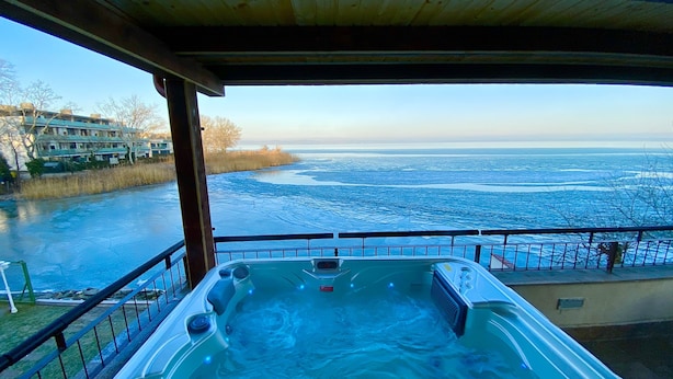 A hot tub with a view of a frozen lake and buildings in the background. - Royal Mediterran Hotel (Siófok)