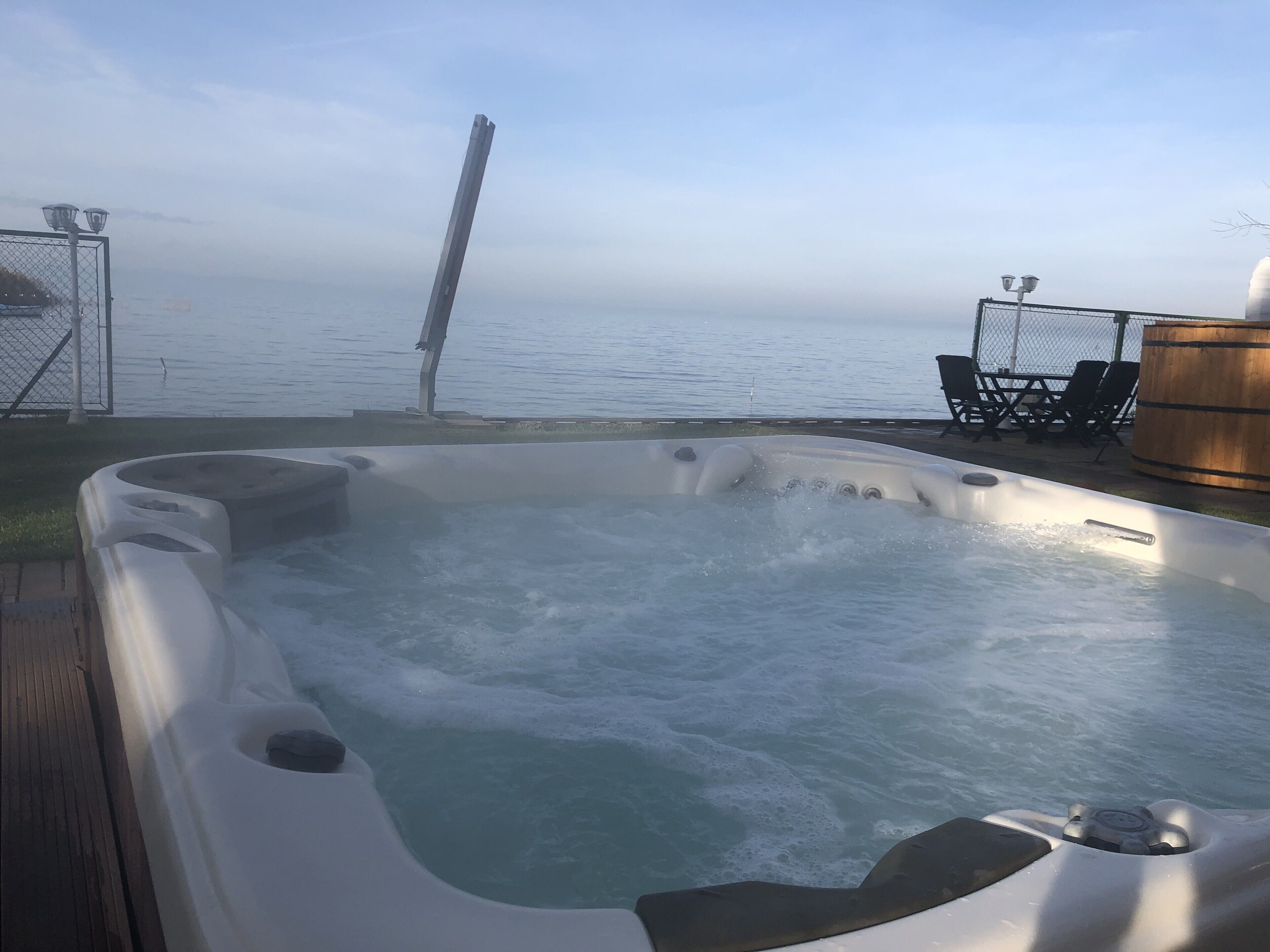 A hot tub with a view of the sea, a wooden barrel, and outdoor furniture.