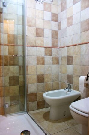 A bathroom with a glass shower enclosure, a bidet, and a toilet.