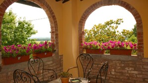 A patio with two brick arches, each with a flower box containing pink flowers. There are two metal chairs and a table with a potted plant. - Stunning private villa for 6 guests with private pool, TV, pets allowed and parking (Castiglion Fiorentino)