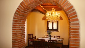 A dining area with a brick archway, a chandelier, a table set for four, and a window with lace curtains. - Stunning private villa for 6 guests with private pool, TV, pets allowed and parking (Castiglion Fiorentino)