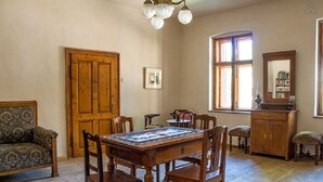 A dining room with a wooden table, chairs, a sofa, a wooden cabinet, and a window with curtains. - Casa Arthur (Biertan)