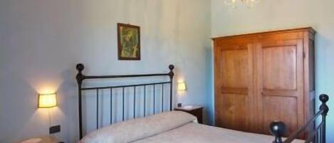 Een slaapkamer met een houten plafond, een bed met een witte dekbedovertrek, een houten garderobe en een vloerkleed met een patroon.