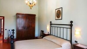 Quarto com teto de madeira, cama com colcha branca, guarda-roupa de madeira, lustre e tapete estampado.
