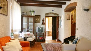 Ein gemütliches Wohnzimmer mit Holzbalkendecke, einem Fernseher und einem Essbereich mit Tisch und Stühlen.