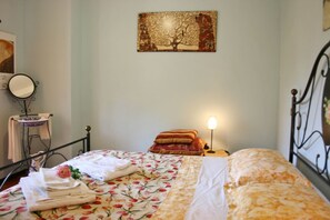 A bedroom with a bed, a bedside table with a lamp, a mirror, and a wall-mounted artwork.