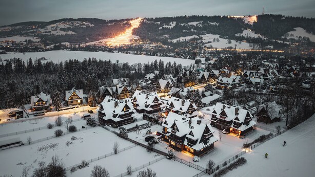 Un village enneigé, avec ses maisons traditionnelles en bois, une piste de ski et une montagne lointaine illuminée.