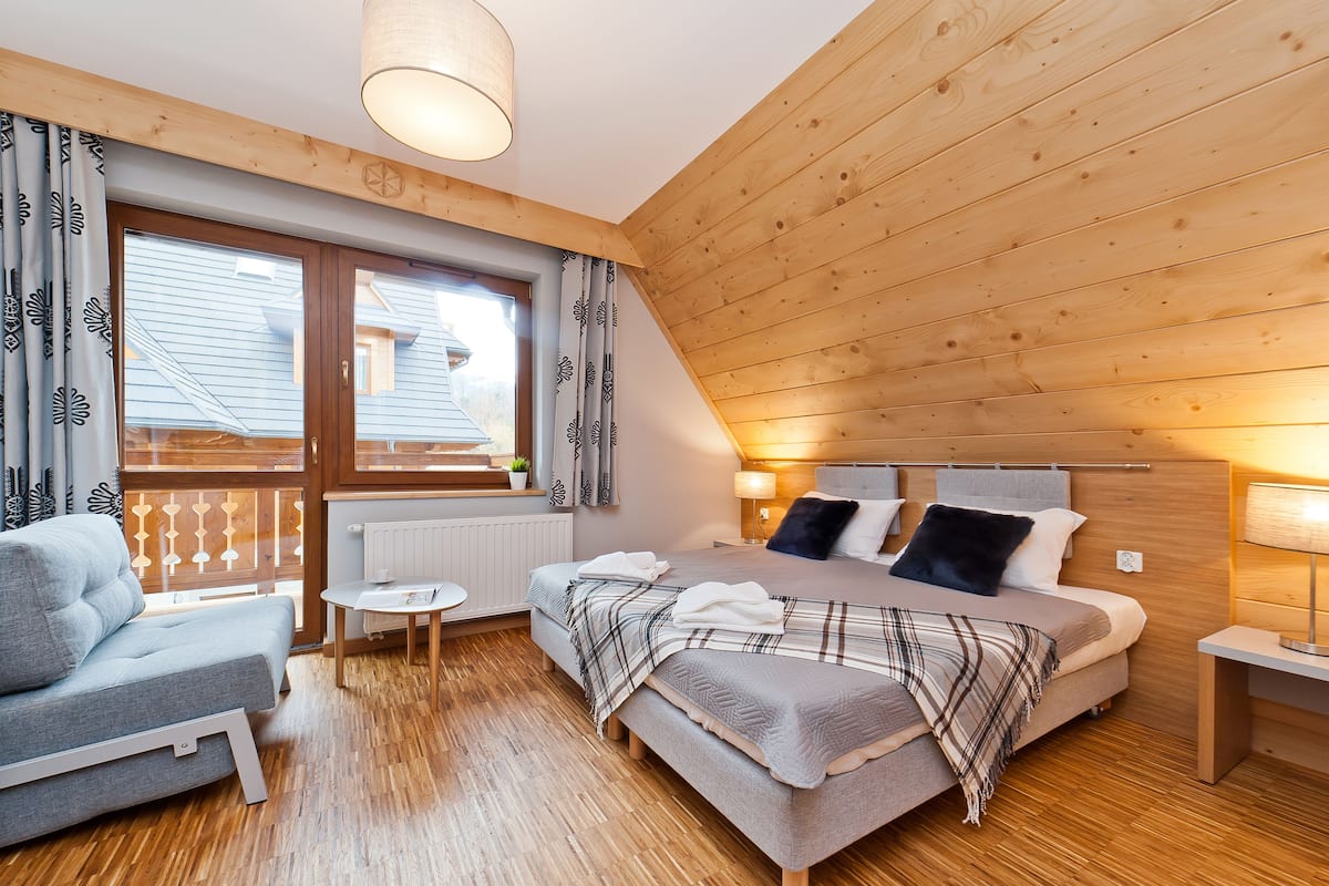 Une chambre confortable avec un lit, une chaise, une petite table et une fenêtre avec des rideaux.