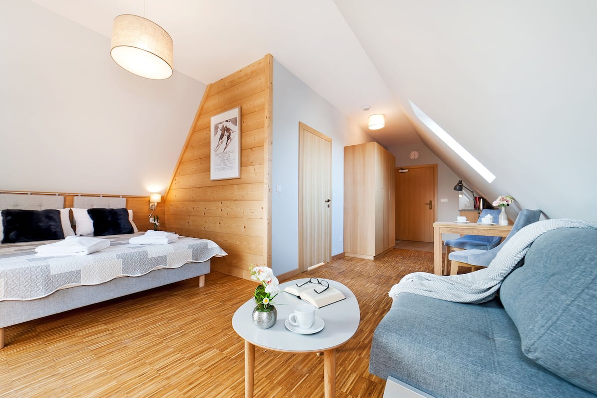 Une chambre moderne avec un lit en mezzanine, un canapé, une petite table avec un vase et un livre, et un plancher en bois.