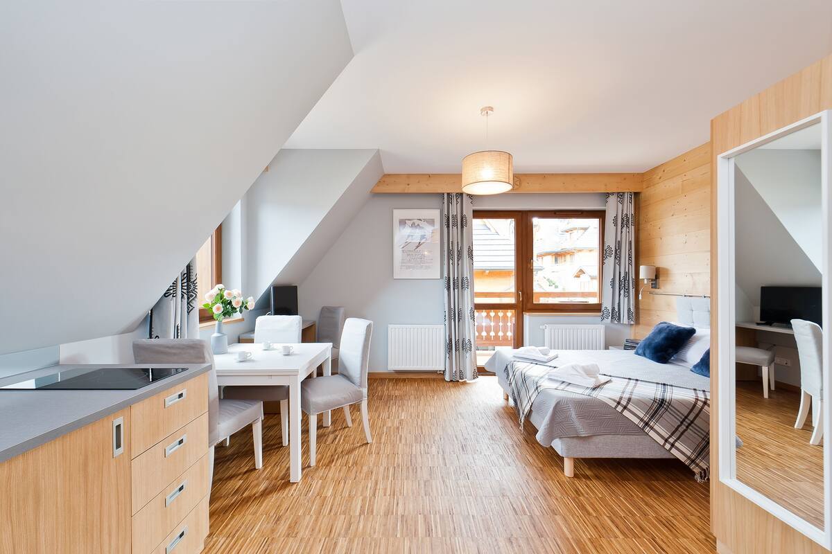 Une pièce moderne et bien éclairée, comprenant un coin repas, un lit recouvert d’une couverture à carreaux et un téléviseur placé dans un coin.
