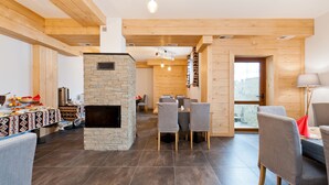 Un intérieur moderne agrémenté d’une cheminée en pierre, de poutres en bois et d’un coin repas avec des chaises grises.