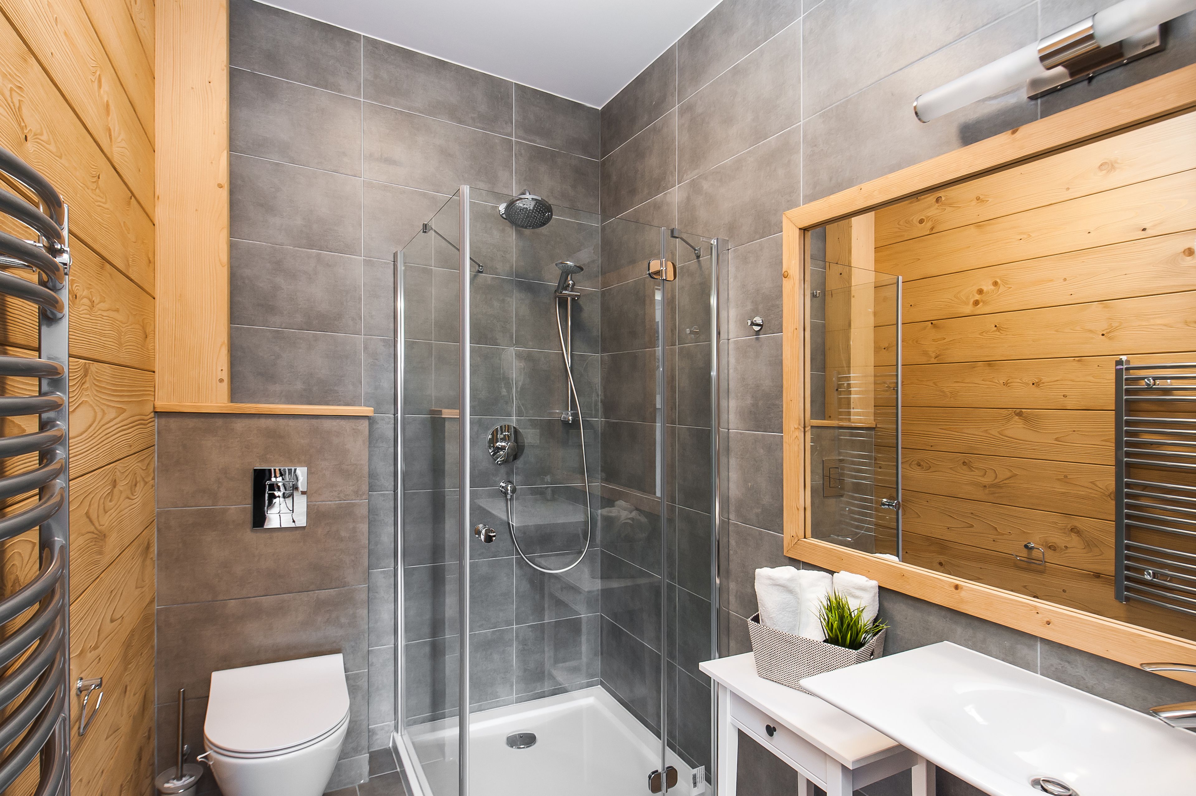 A modern bathroom with a glass-enclosed shower, a white toilet, and a wooden vanity with a mirror.
