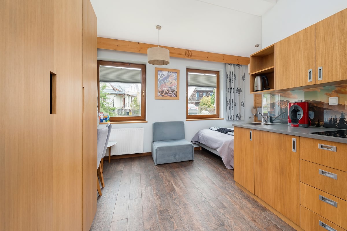 Une cuisine compacte avec des meubles en bois, une cuisinière encastrée et une fenêtre donnant sur une maison.