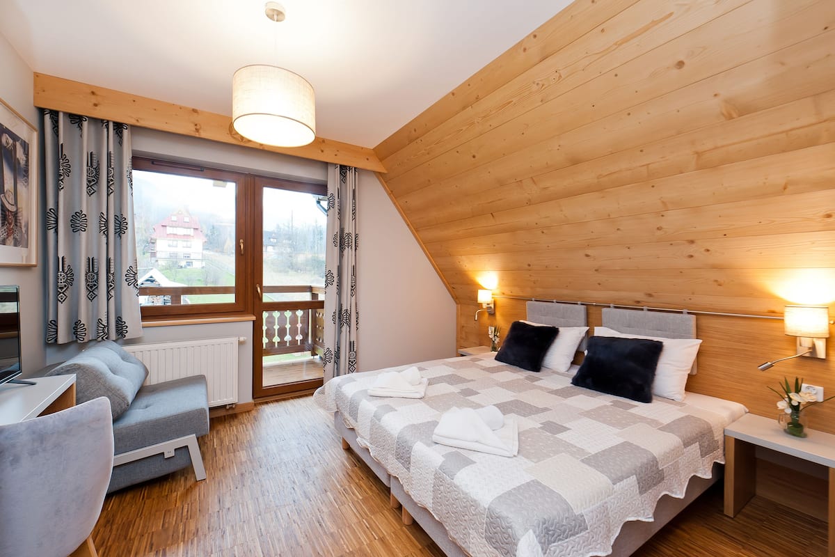 Une chambre avec un plafond en bois, un lit recouvert d’une couverture à carreaux, un bureau et une chaise.
