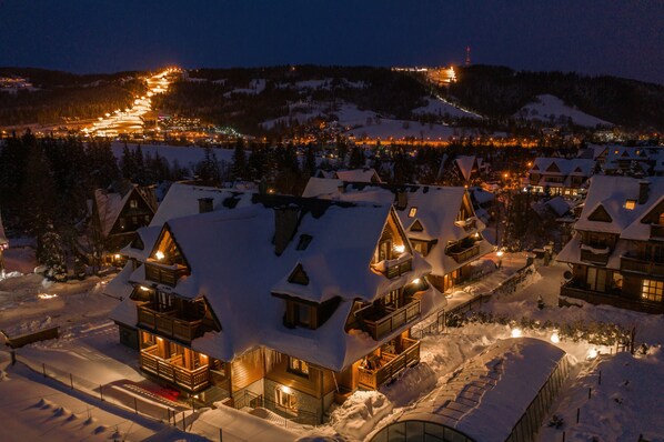 A snow-covered lodge with multiple balconies and a lit pathway leading to the entrance. - Sun & Snow Resorts Lipki Park (Zakopane)