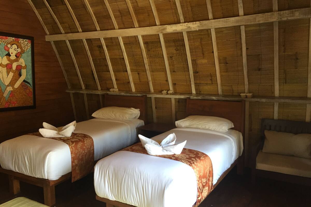 A room with two beds, wooden beams on the ceiling, and a painting on the wall.