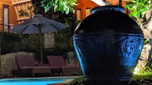 Una urna decorativa gran al costat d'una piscina, amb gandules i una ombrel·la al fons.