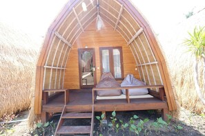A wooden A-frame structure with a bench and cushions, a door, and a small staircase leading up.