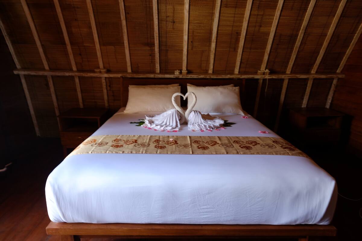 A bed with a white bedspread and two swan-shaped pillows.