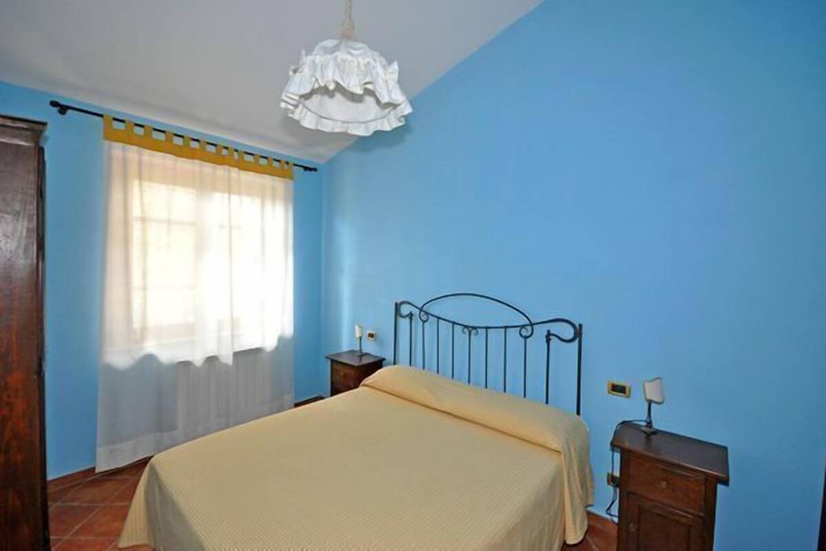 Une chambre à coucher avec un lit, une table de chevet, une lampe et une fenêtre avec des rideaux.