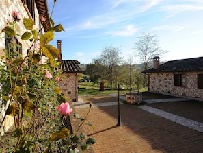 A stone building with a tiled roof, a brick pathway, and a rose bush in the foreground.