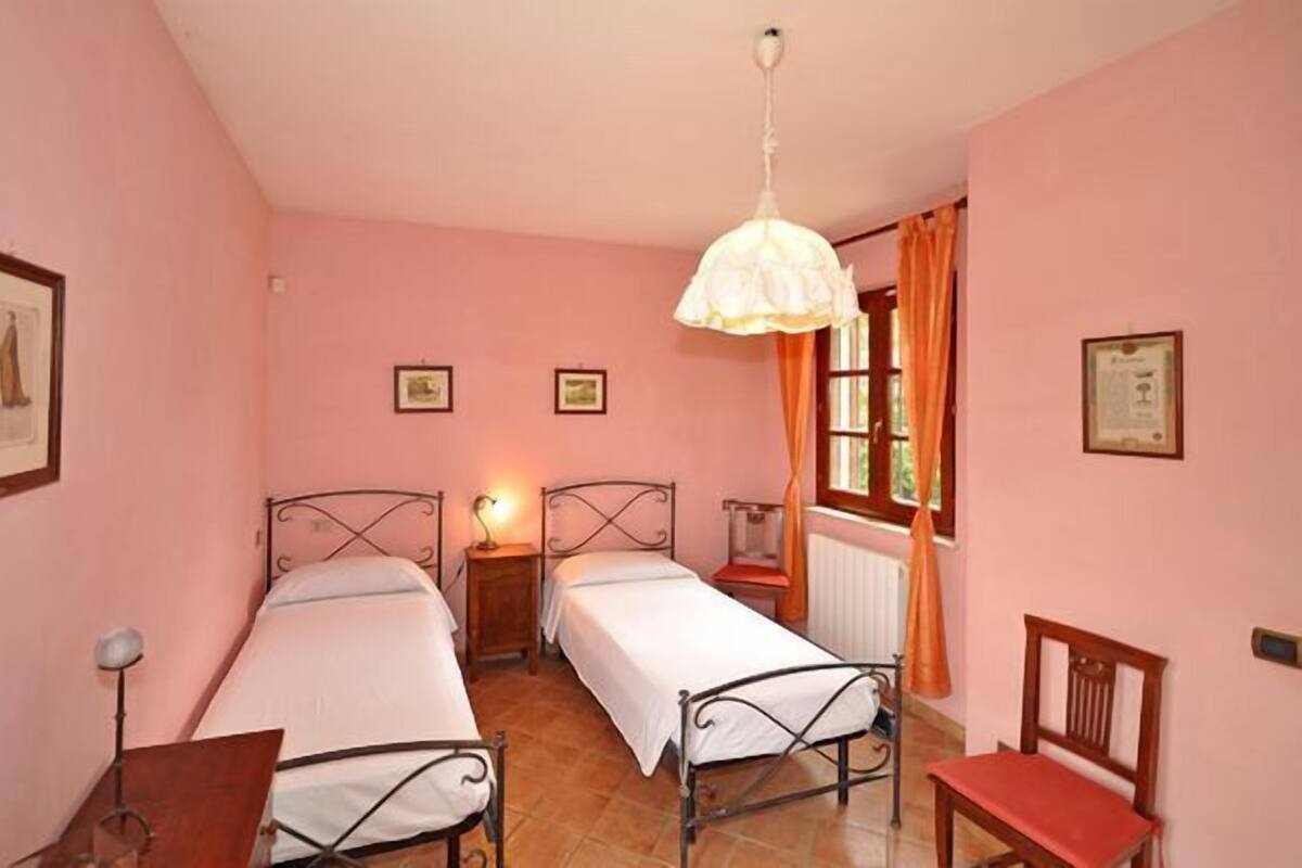 Une chambre avec deux lits simples, une chaise en bois, un bureau et un luminaire suspendu.