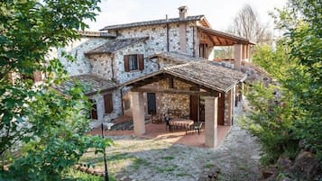 Una casa de piedra con un patio, una zona de estar cubierta al aire libre y vistas de la vegetación circundante.