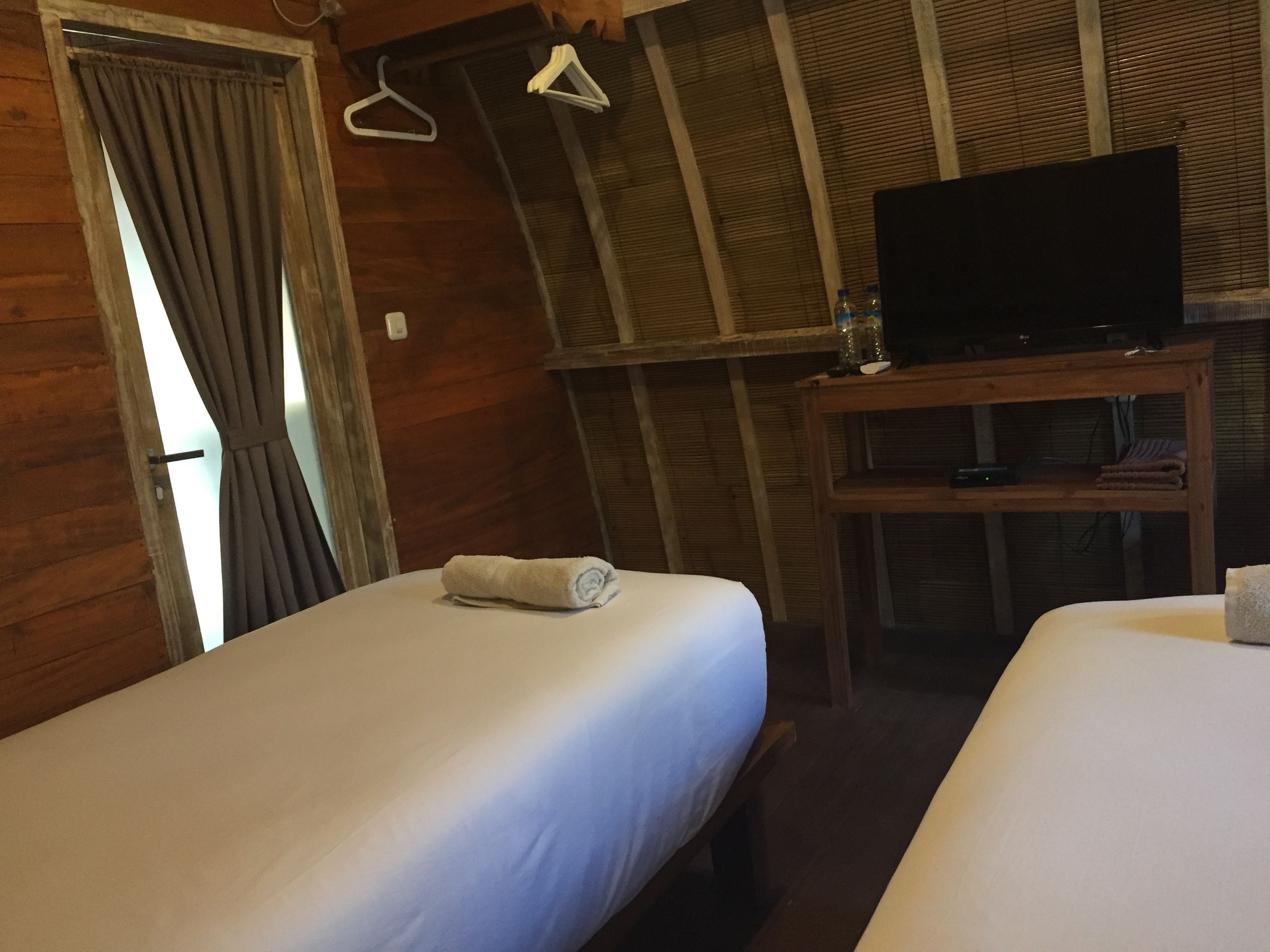 A wooden room with two beds, a television on a wooden stand, and a window with curtains.