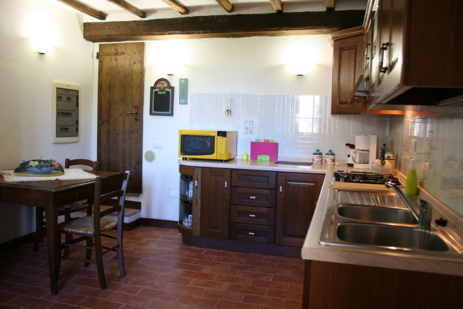 A kitchen with wooden cabinets, a yellow microwave, a sink, and a dining area with a table and chairs.